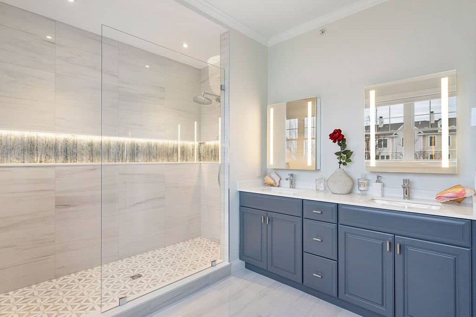 Well-lighted modern bathroom with a glass-enclosed shower, dual sinks, gray cabinets, and light gray walls