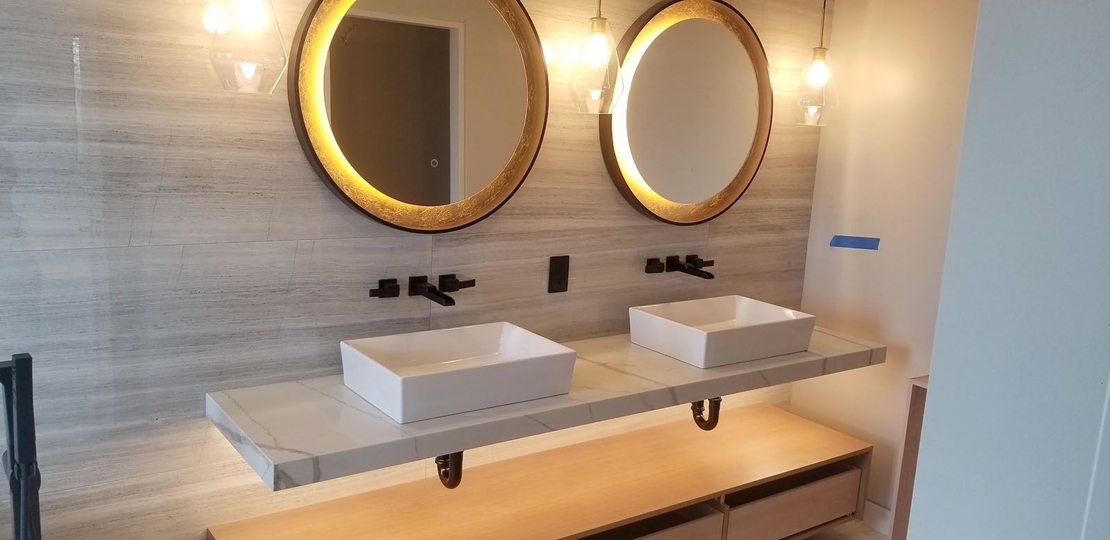 Well-lighted modern bathroom with two round mirrors, vessel sinks, and wood vanity