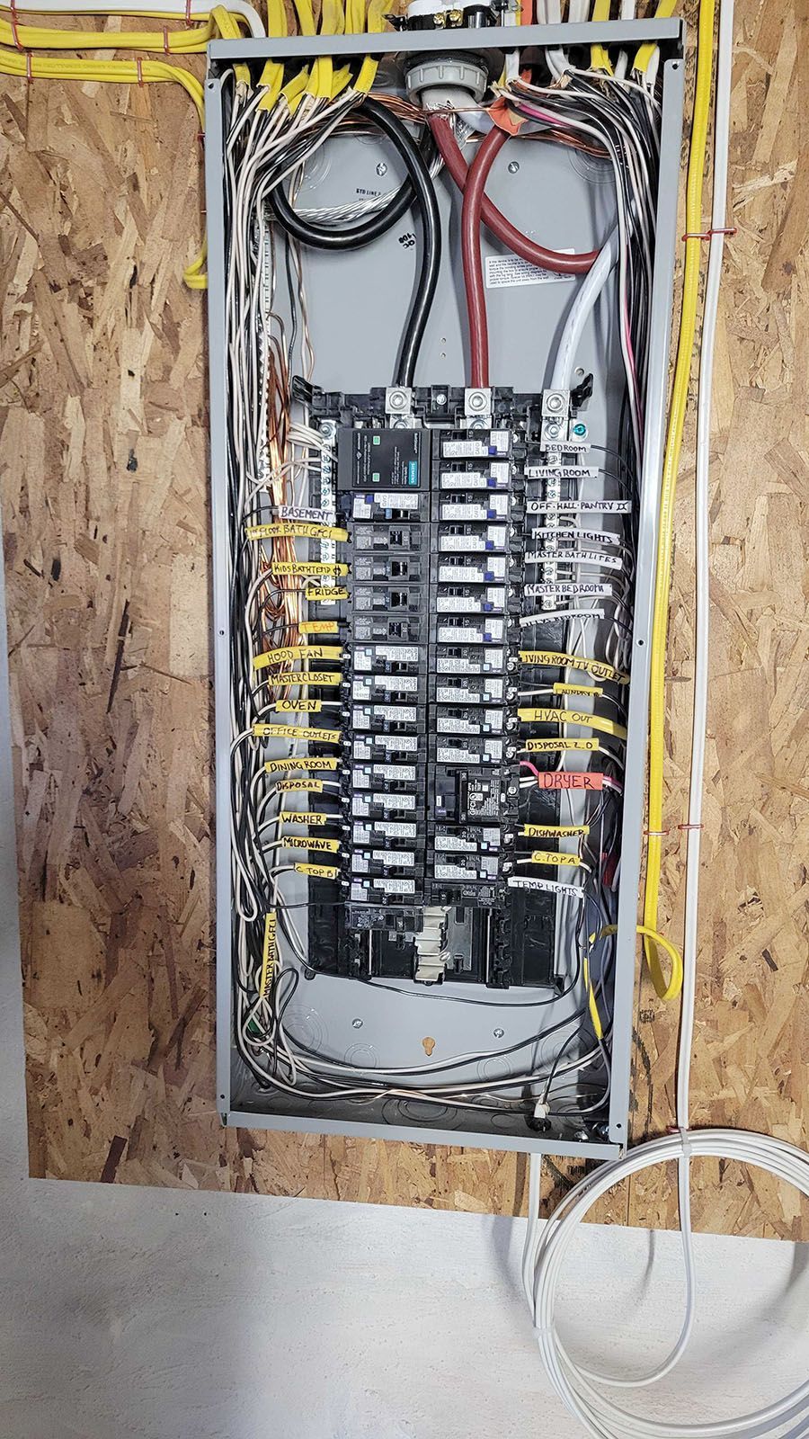 Electrical panel with numerous wires and circuit breakers, mounted on a wood panel