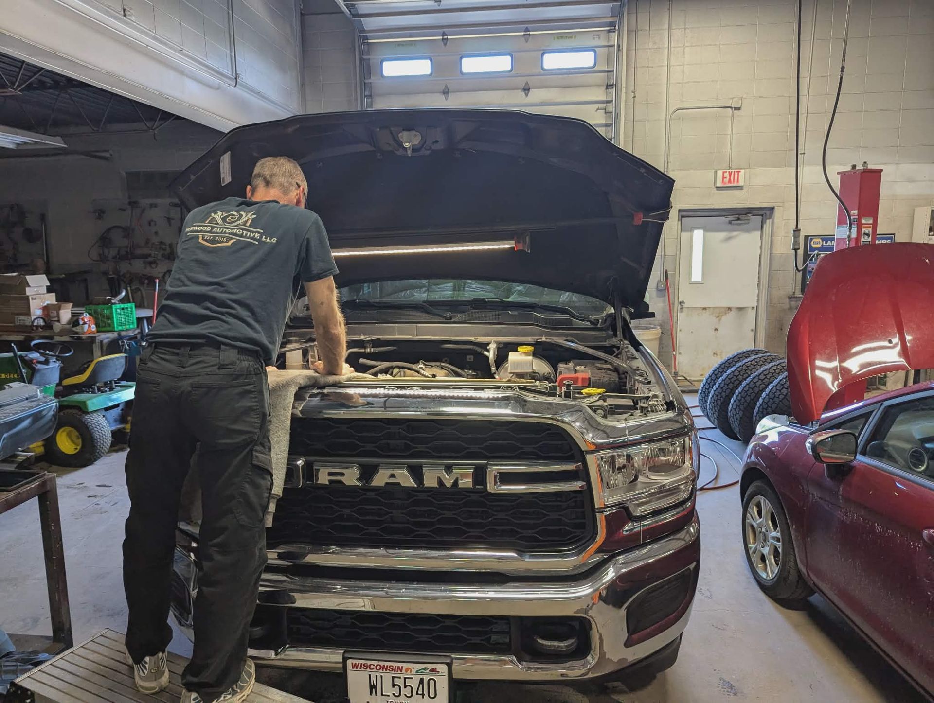 Mechanic working under the open hood of a black RAM truck in an auto shop