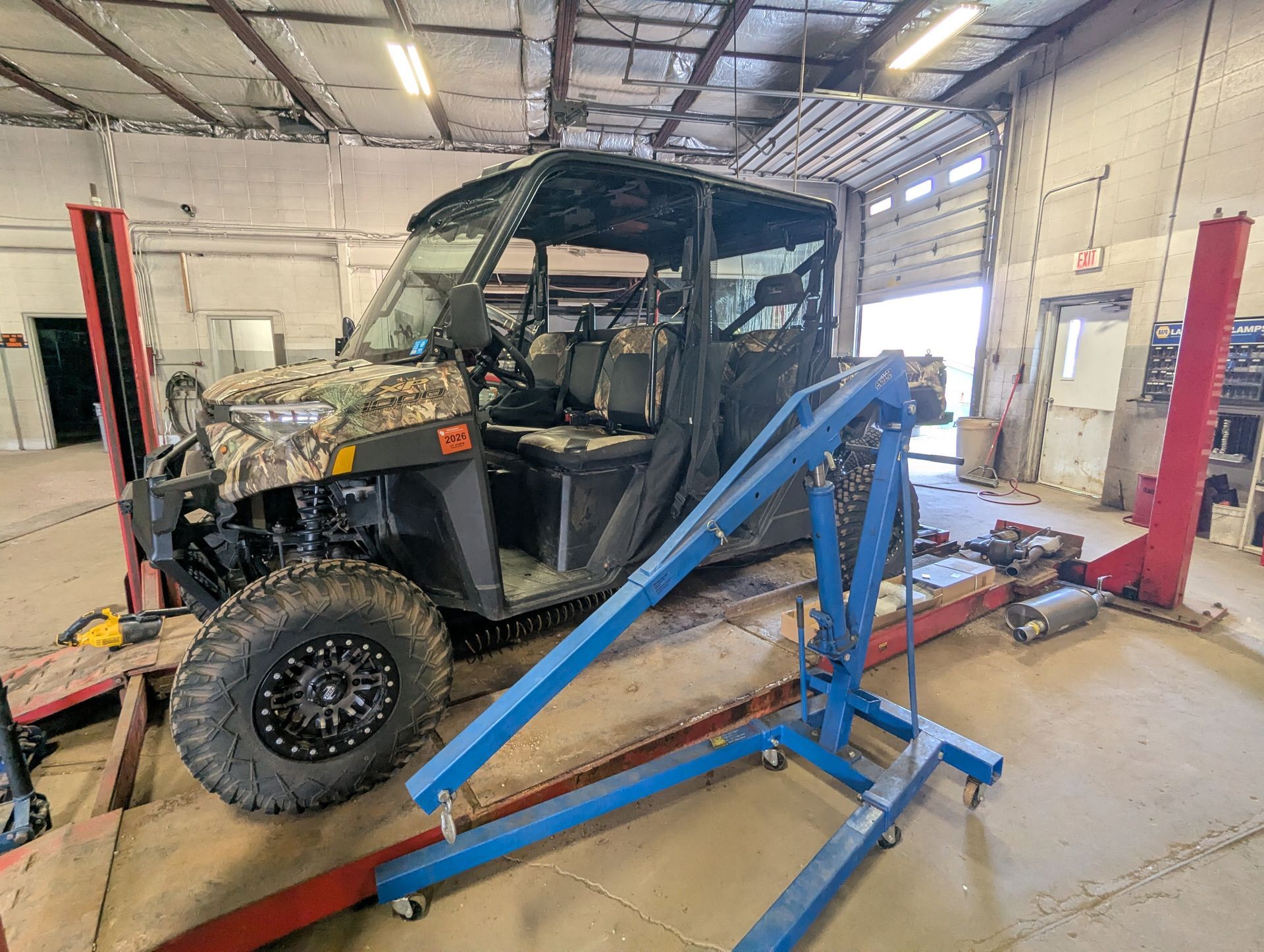 ATV on a blue vehicle lift inside an auto repair shop, with another vehicle in the background