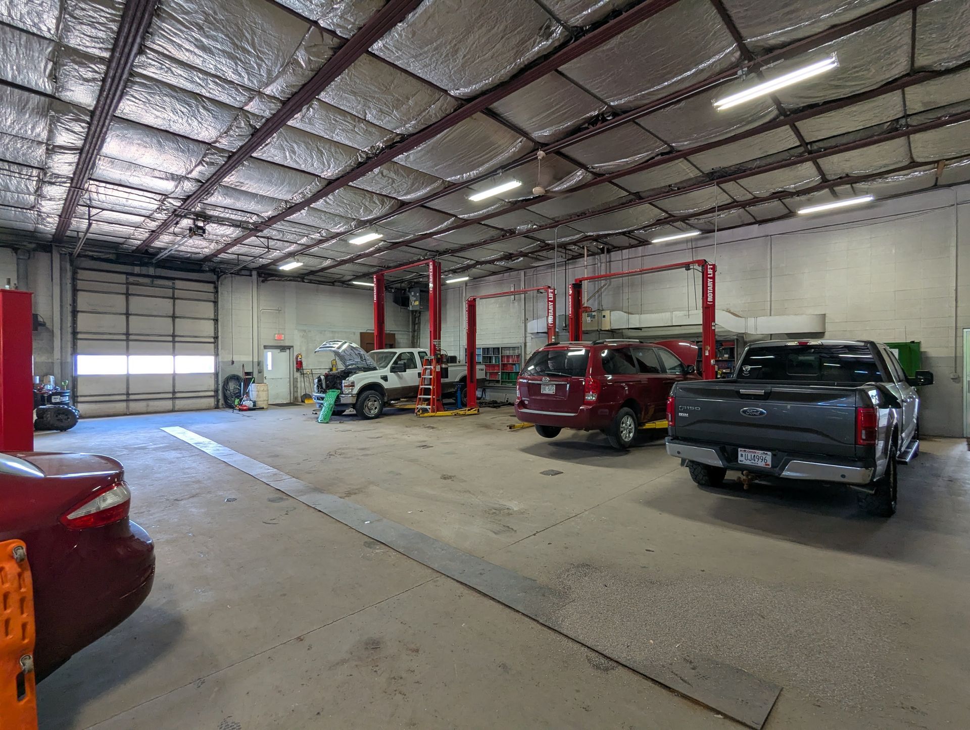 Auto repair shop interior with several vehicles parked under red lifts and a high metal ceiling