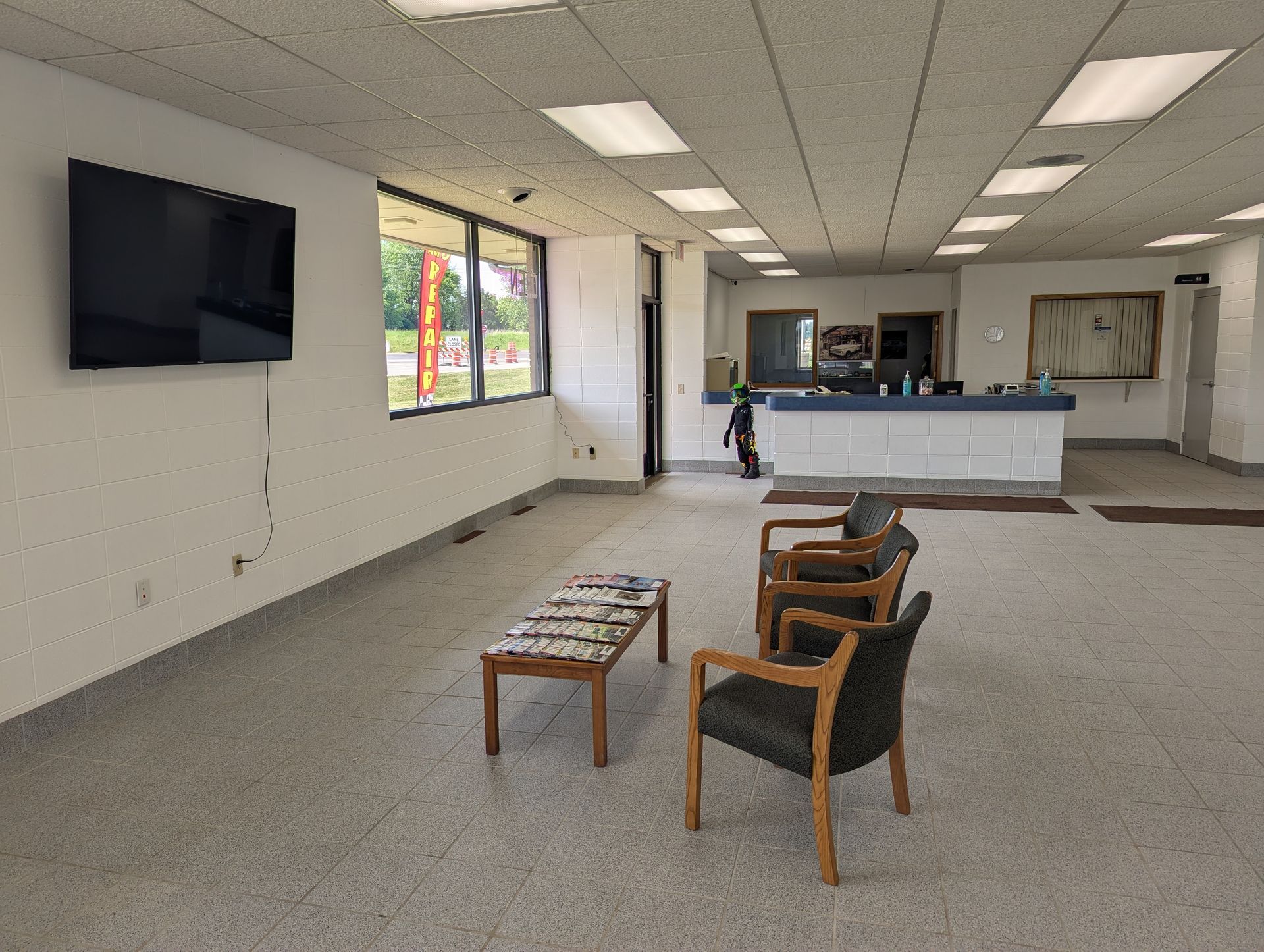 Empty office lobby with a wall-mounted TV, chairs, small table, and a reception desk.