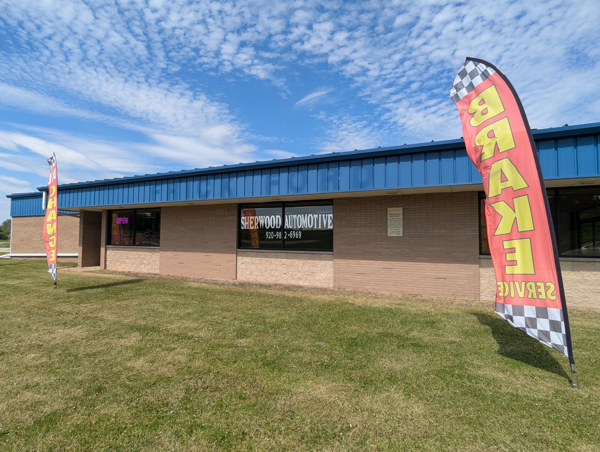 Small brick building with blue roof and colorful “GRAND OPENING” banners under a cloudy sky