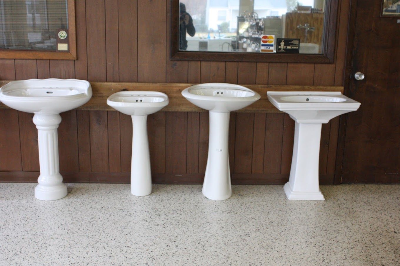 Four white pedestal sinks are lined up in a room