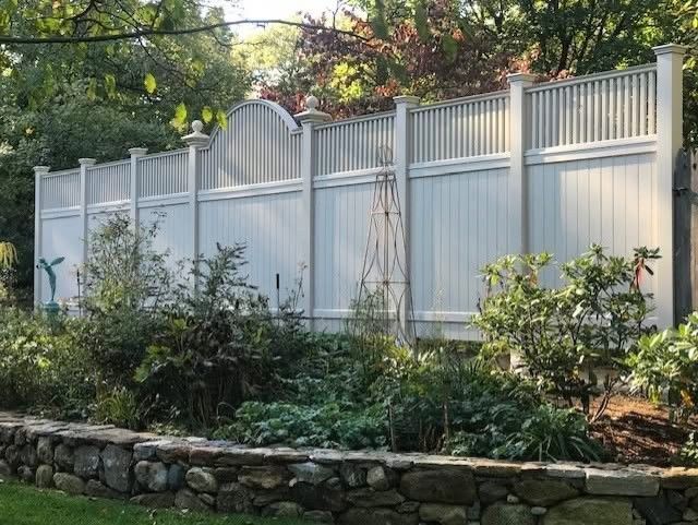 White vinyl fence with stone wall, garden plants in foreground.