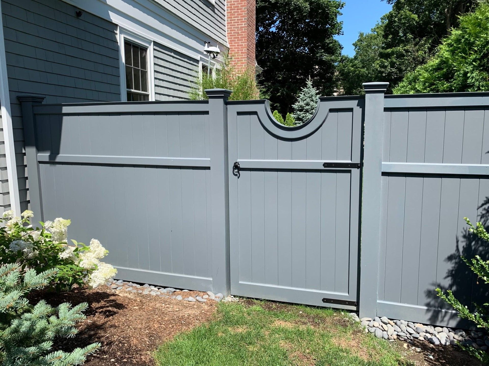 Gray wooden fence with gate; lush greenery on either side.