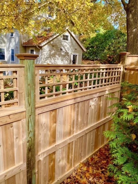 Wooden privacy fence with lattice top in a leafy yard, autumn foliage and a house in the background