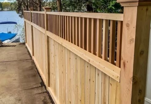 Wooden privacy fence with top railing along a concrete path beside water