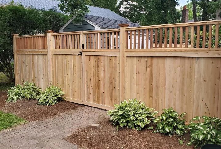 Wooden backyard privacy fence with lattice top, bordered by shrubs and a curved stone path.