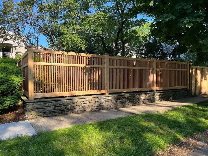 Wooden privacy fence with stone base along a sunny residential sidewalk and green lawn