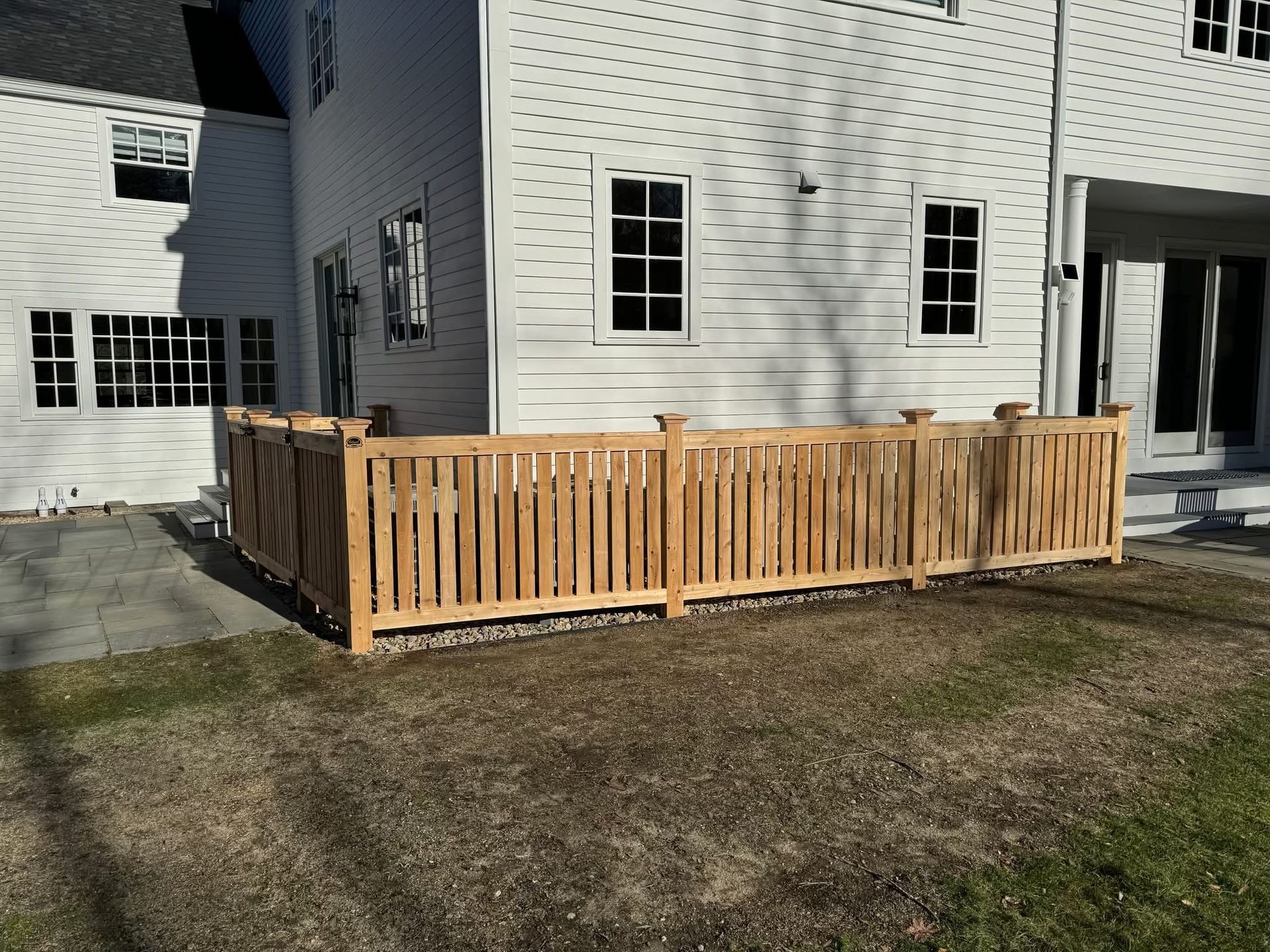 Wooden deck railing around a small patio beside a white house.
