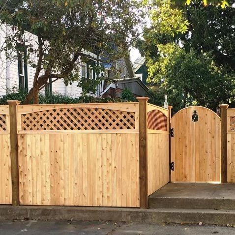 Wooden front fence and gate with lattice detail along a sidewalk, with trees and a house behind it.