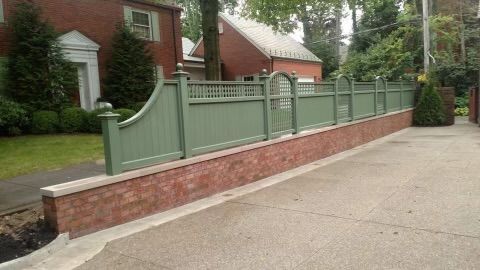 Green fence atop a brick wall beside a driveway in front of a house
