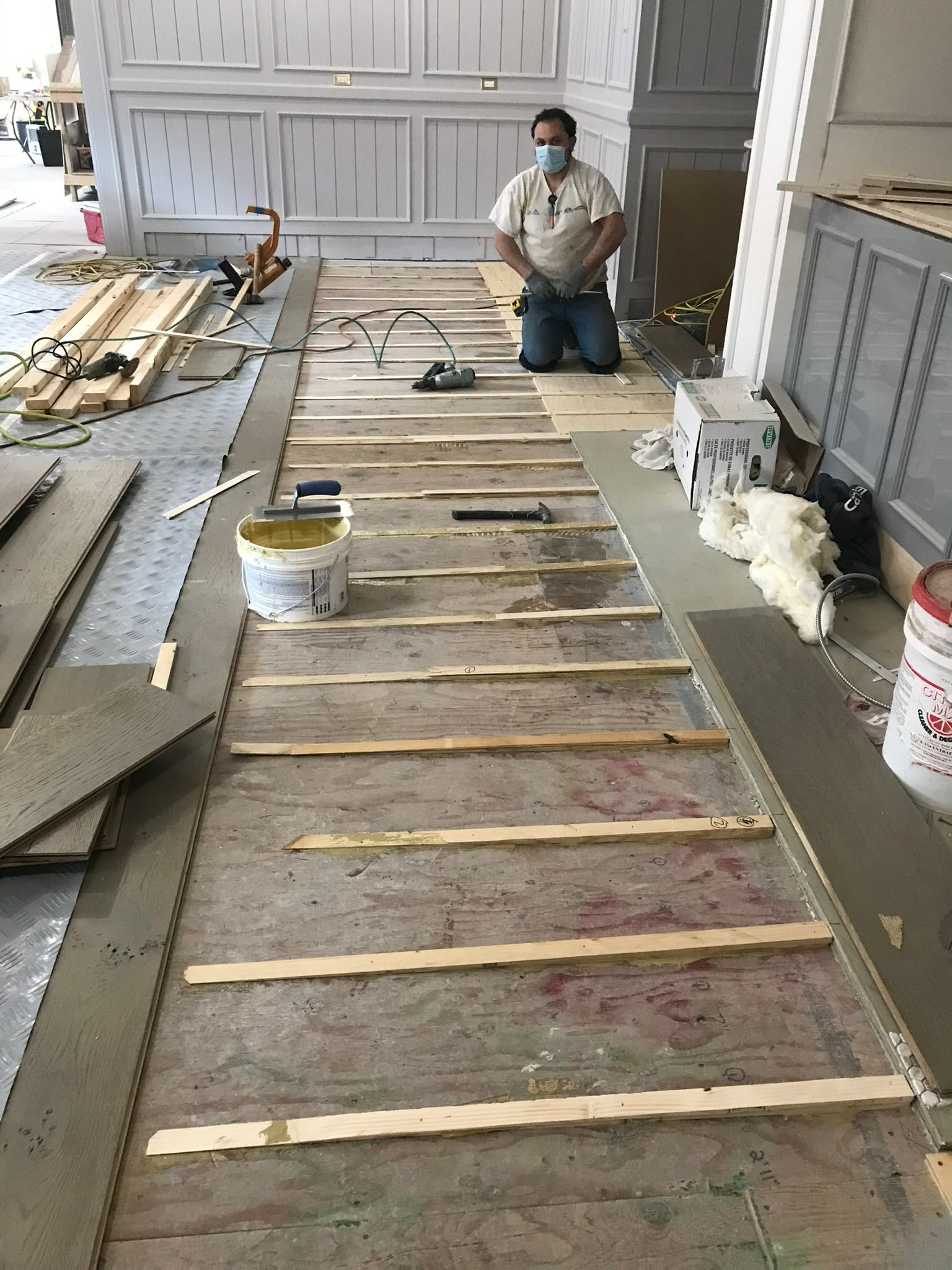 Man kneeling, installing flooring. Boards and tools on concrete floor in a room.