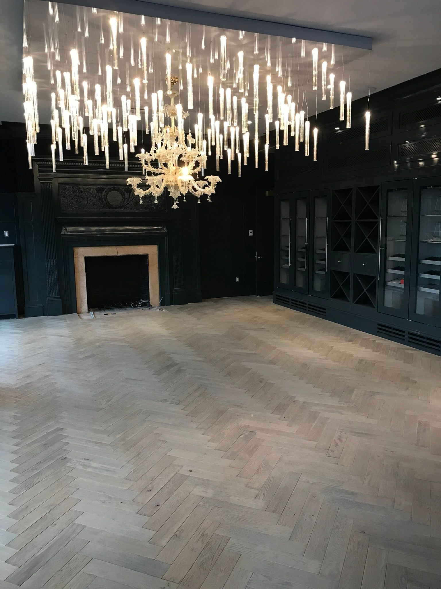 Elegant room with a fireplace, dark walls, large cabinet, chandelier, and a unique light fixture.