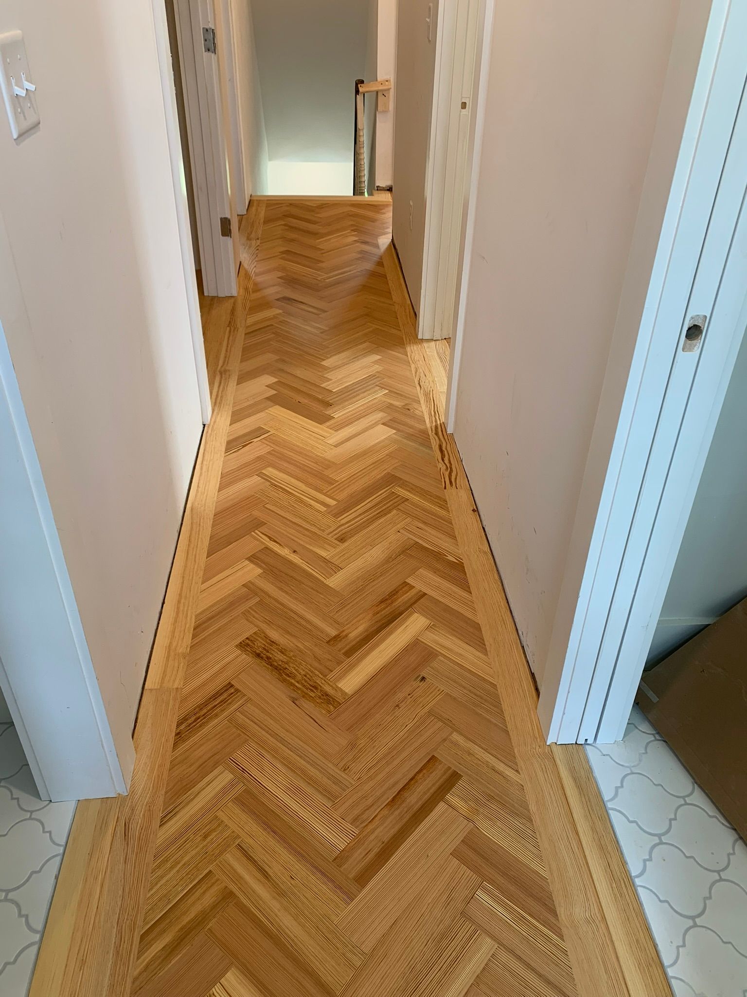 Herringbone wood floor in a hallway with white walls and doors.