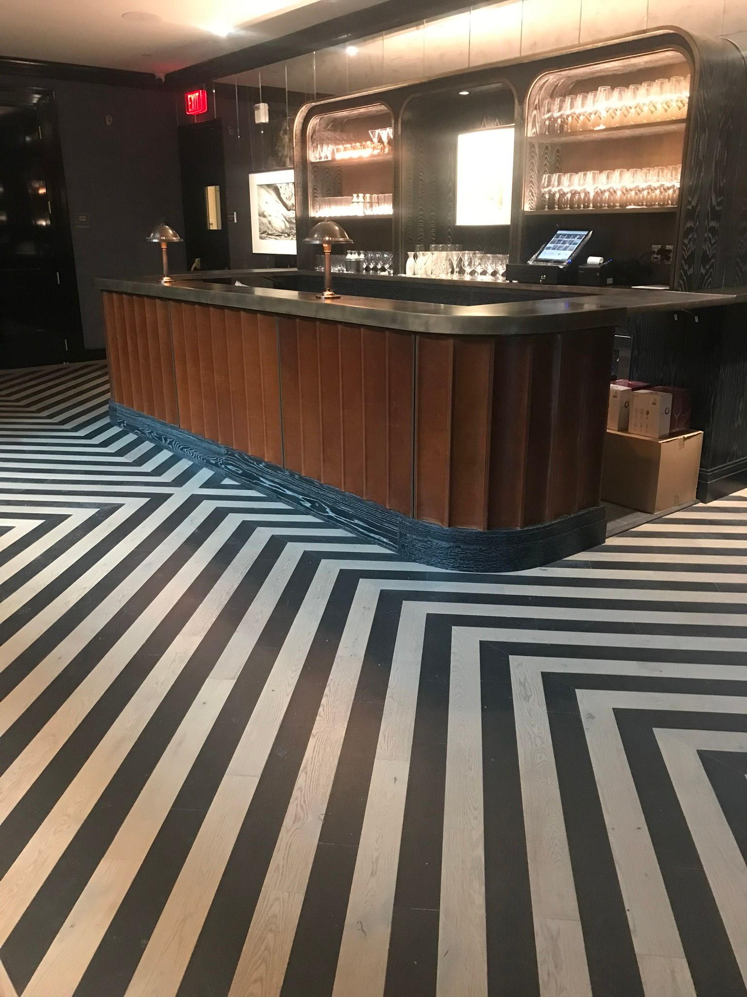 Bar with wooden front, black countertop, geometric black and white floor, shelving in background.