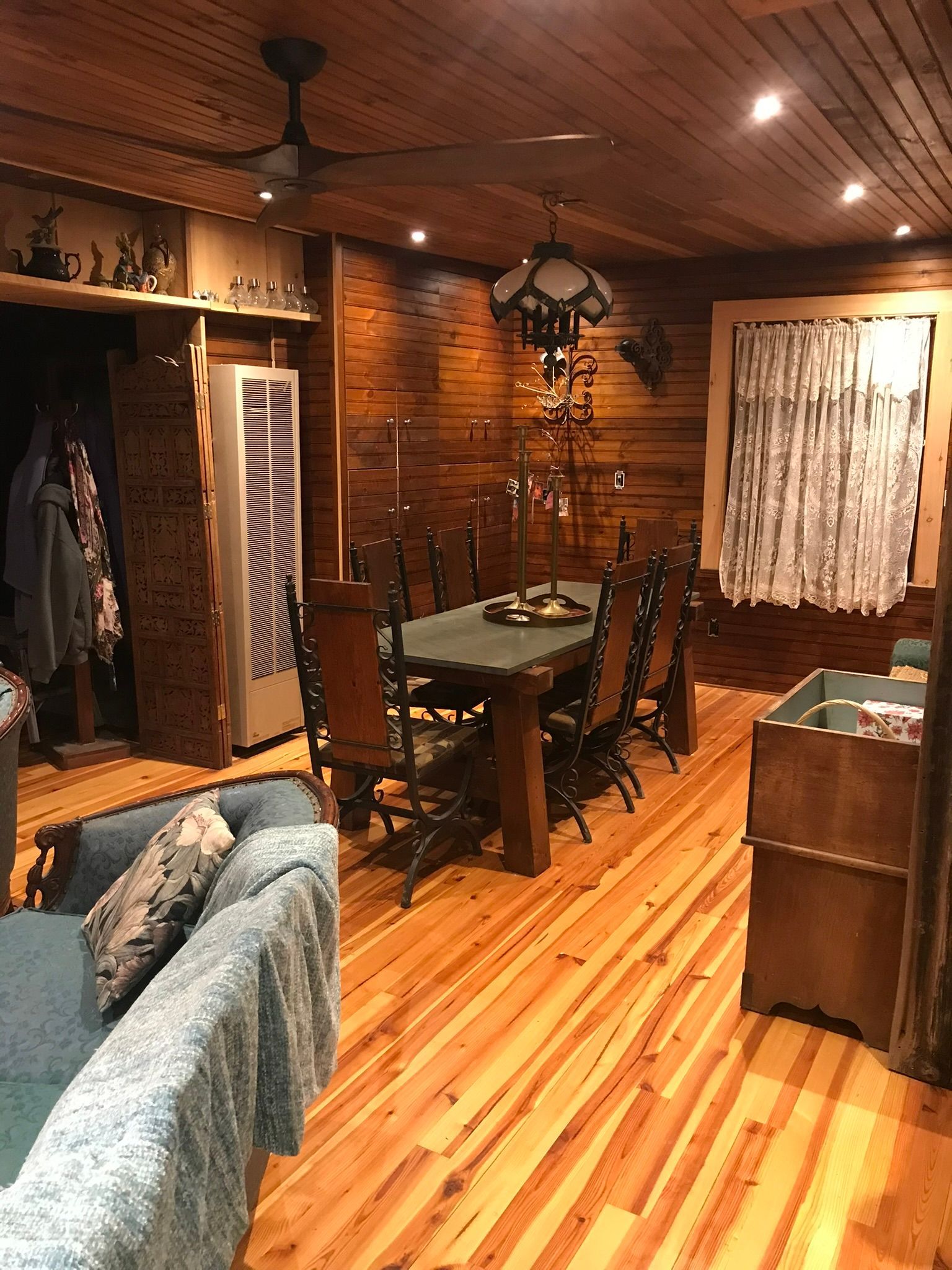 Wooden dining room with a table set for a meal.  Brown wood walls and floor. A couch is visible on the left.