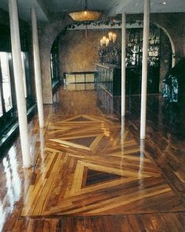 Wooden floor with geometric patterns in a room with white columns and a bar in the background.