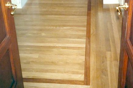 Wooden floor inside doorway, lighter wood within darker border. Gold door handles visible.