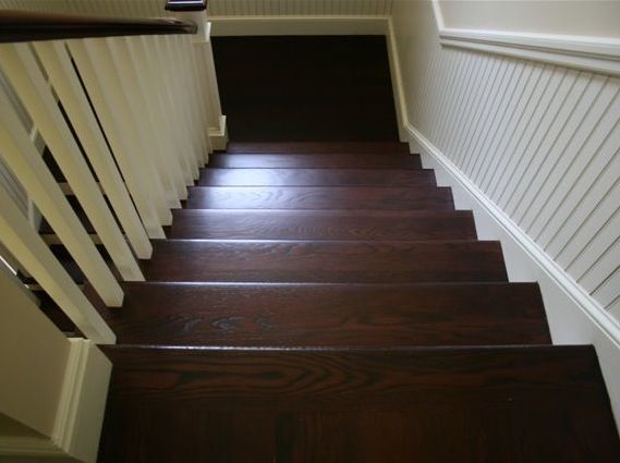 Wooden staircase with dark brown steps, white banister and wall paneling.