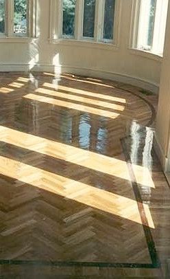 Sunlight streams across a polished parquet wood floor in a room with curved windows.