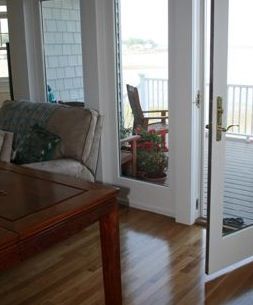 Living room with hardwood floors, sofa, and a table. French doors open to a deck.