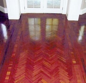 Polished, dark wood parquet floor in a herringbone pattern reflecting light and a double door.