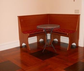 Corner booth with wooden benches, red cushions, and round table on a wood floor.