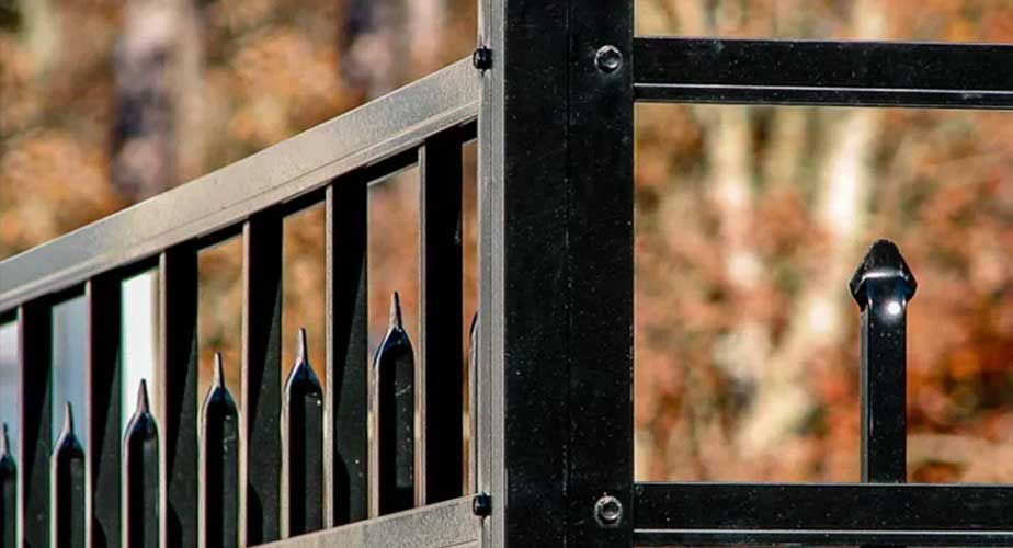 A close up of a black metal fence with trees in the background.