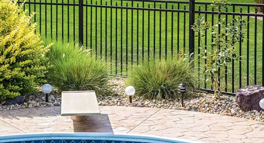 A fence surrounds a swimming pool in a backyard.