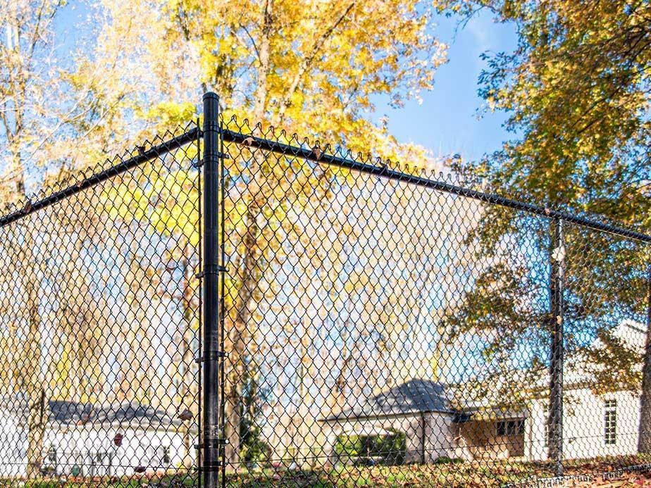 A chain link fence with trees in the background and a house in the background.