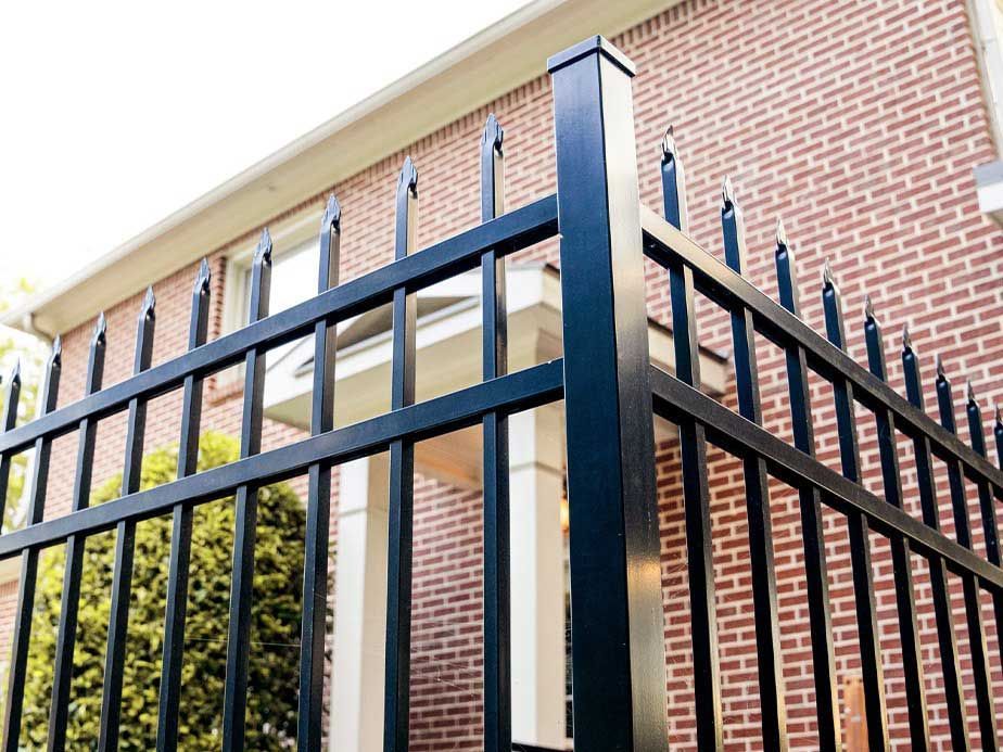 A black metal fence is in front of a brick house.