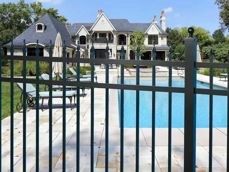 A large house with a swimming pool behind a fence.