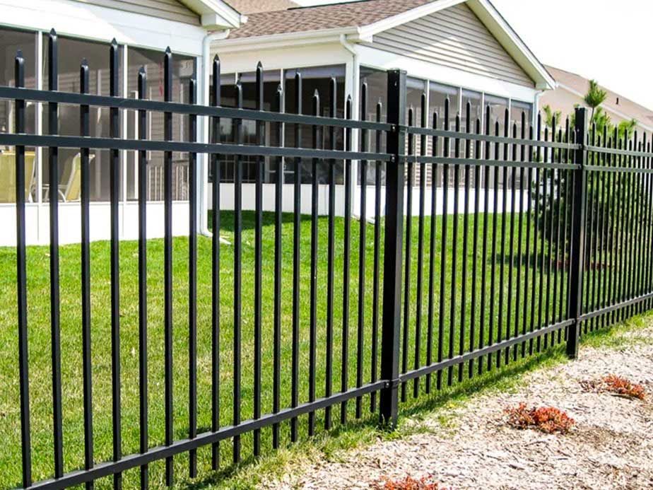 A black metal fence surrounds a lush green yard in front of a house.