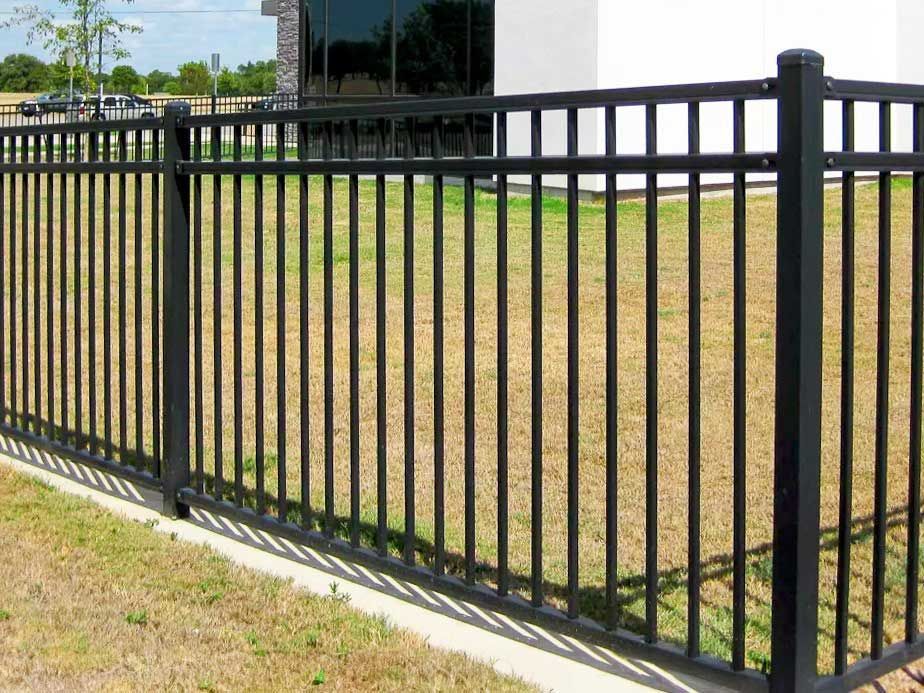 A black metal fence surrounds a grassy field in front of a building.