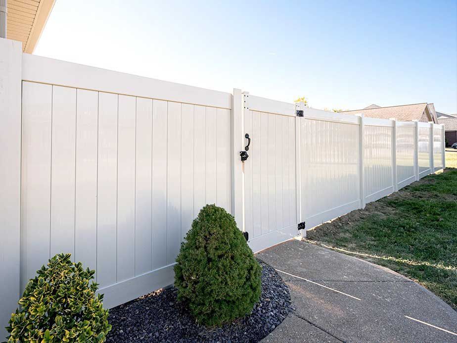 A white vinyl fence with a gate in the backyard of a house.