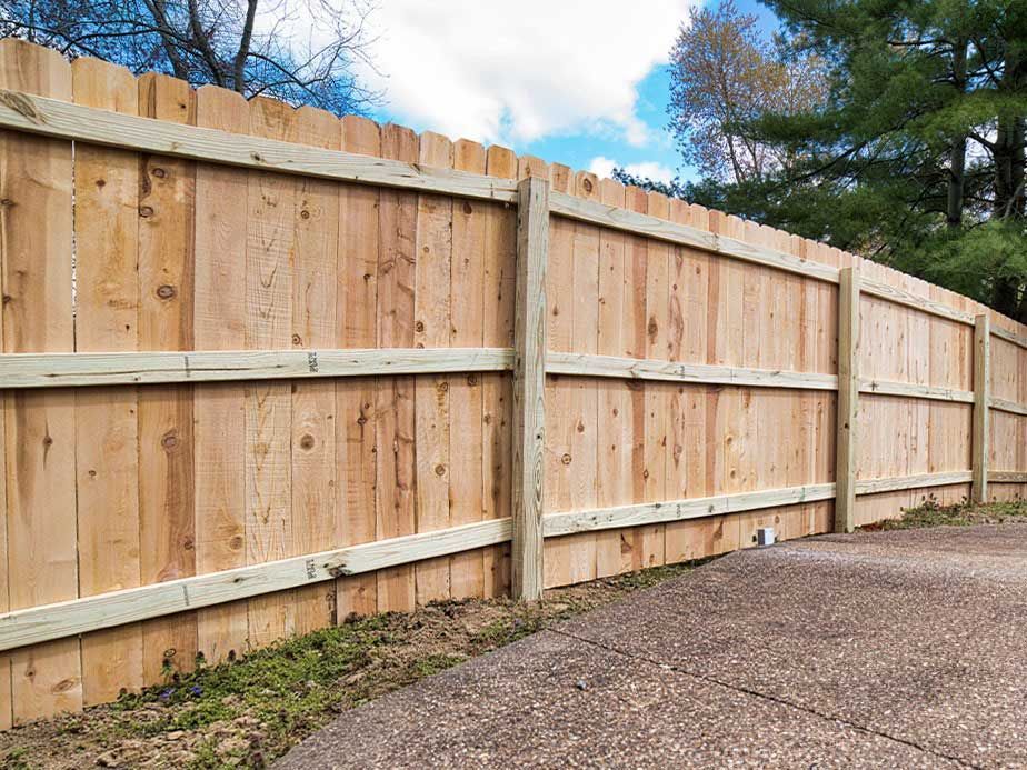 A wooden fence is sitting next to a concrete driveway.