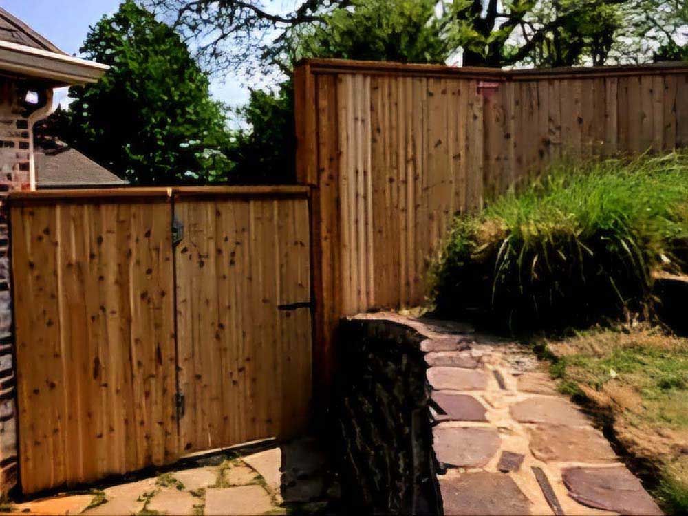 A wooden fence surrounds a stone walkway leading to a house.