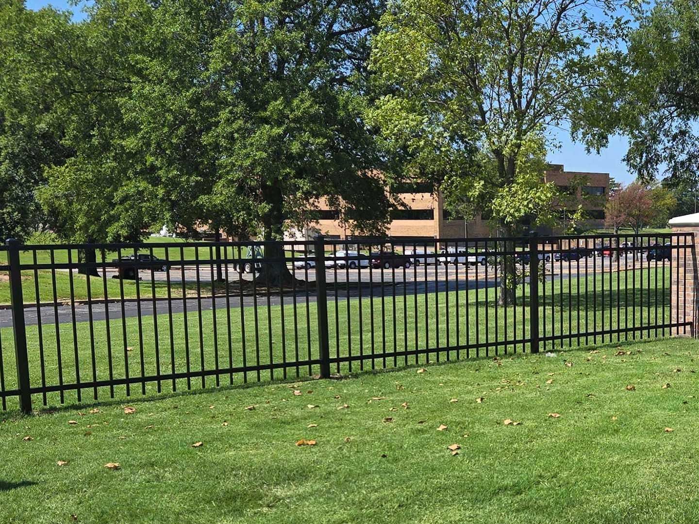 A black fence surrounds a lush green field in a park.