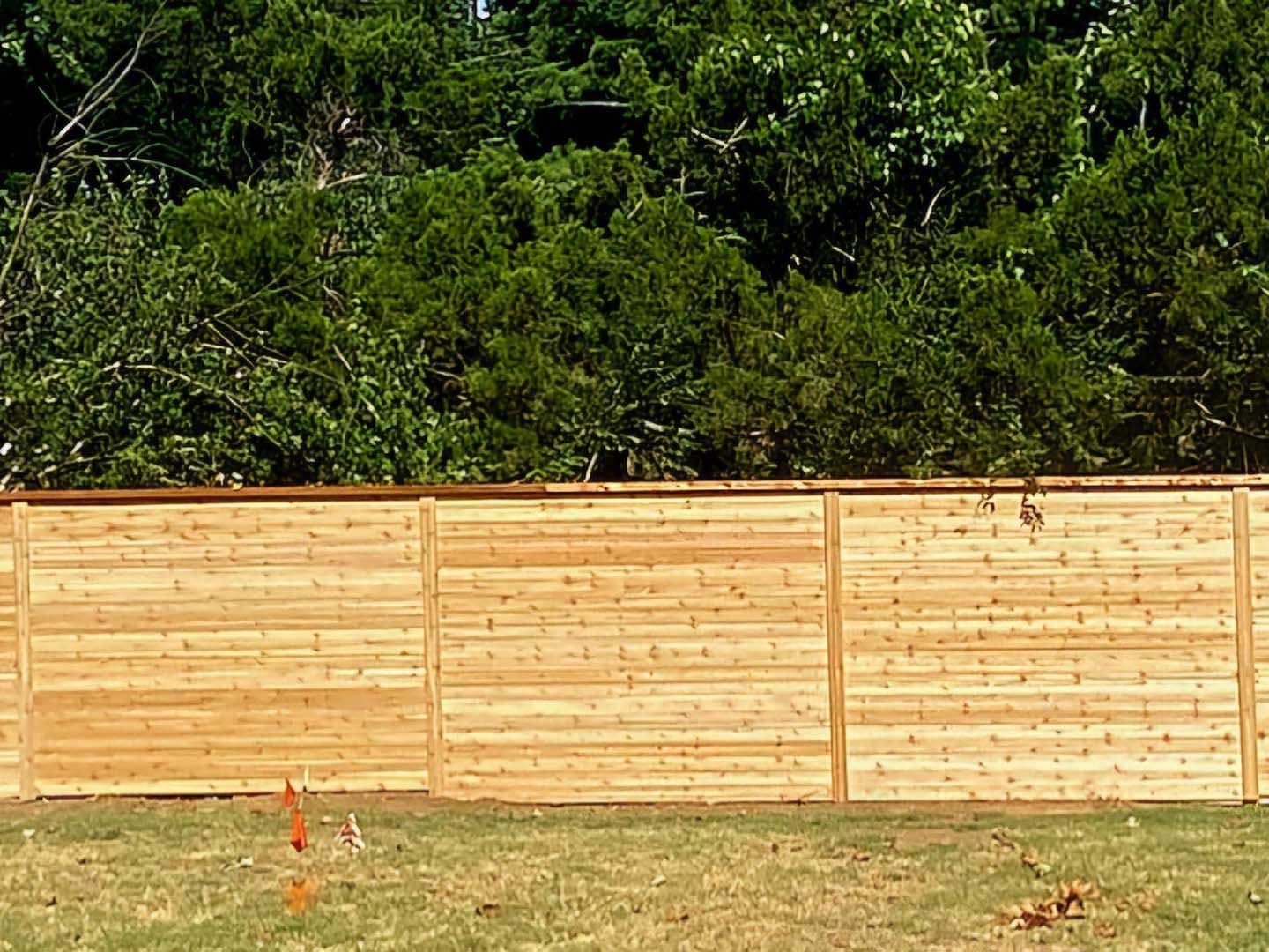 A wooden fence surrounds a lush green field with trees in the background.