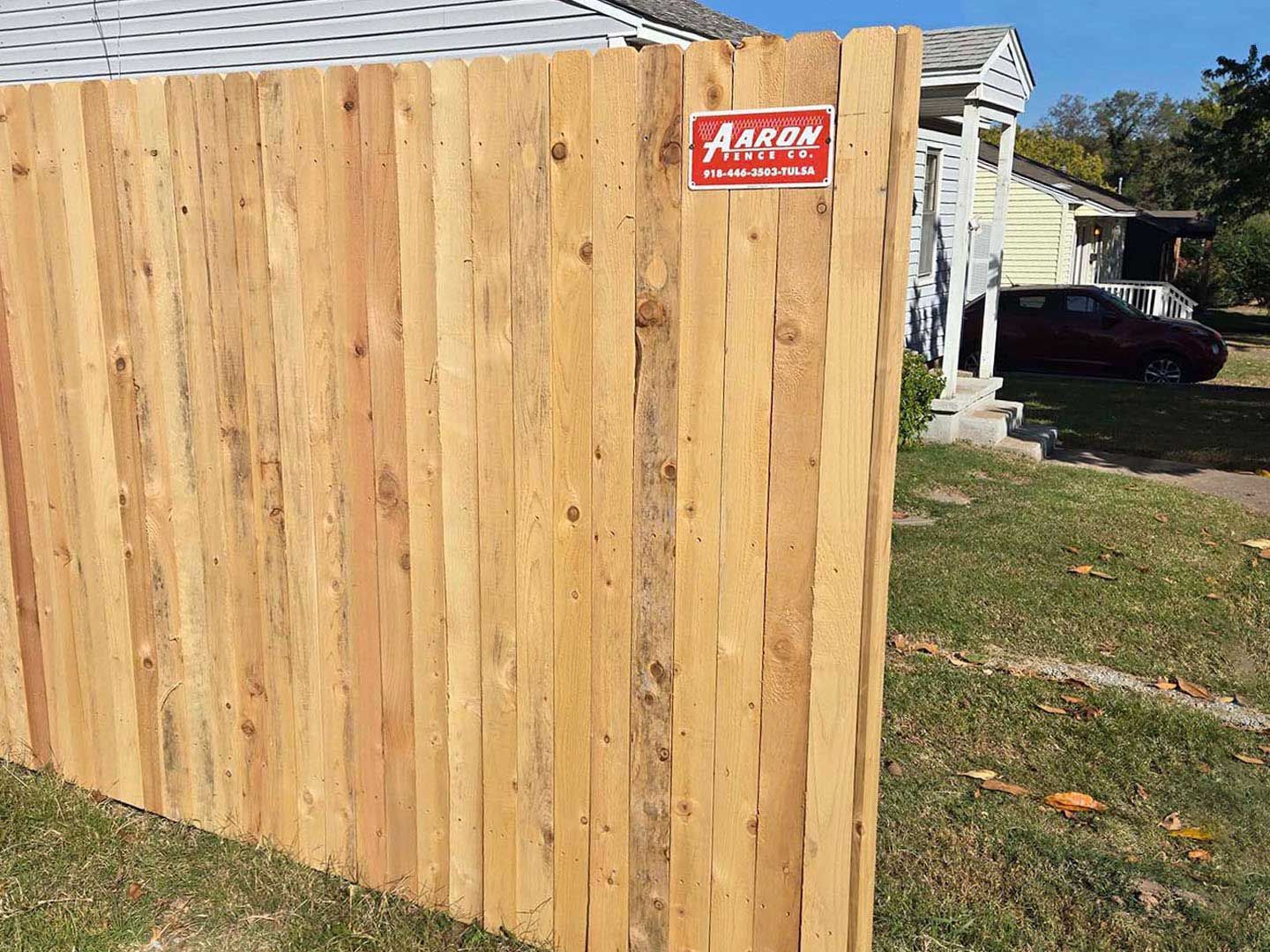 A wooden fence with a sign on it in front of a house.