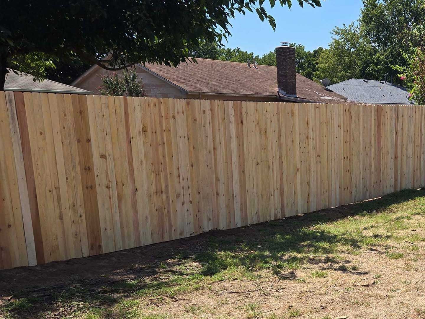 A wooden fence surrounds a yard with houses in the background