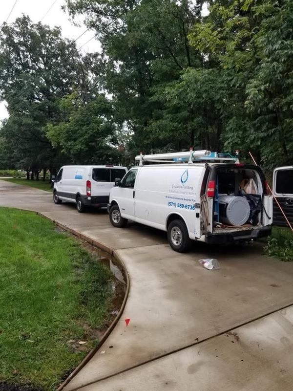 Two white service vans parked in a driveway surrounded by trees, with the back doors of one van open.
