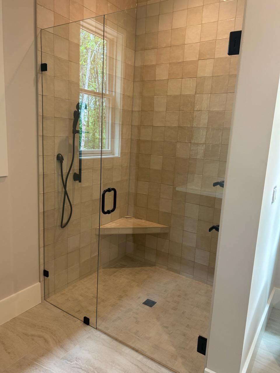 A bathroom with a walk in shower with a glass door and a window.