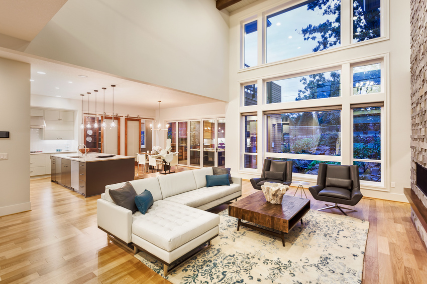 Modern living room with high windows, sectional sofa, and open kitchen.
