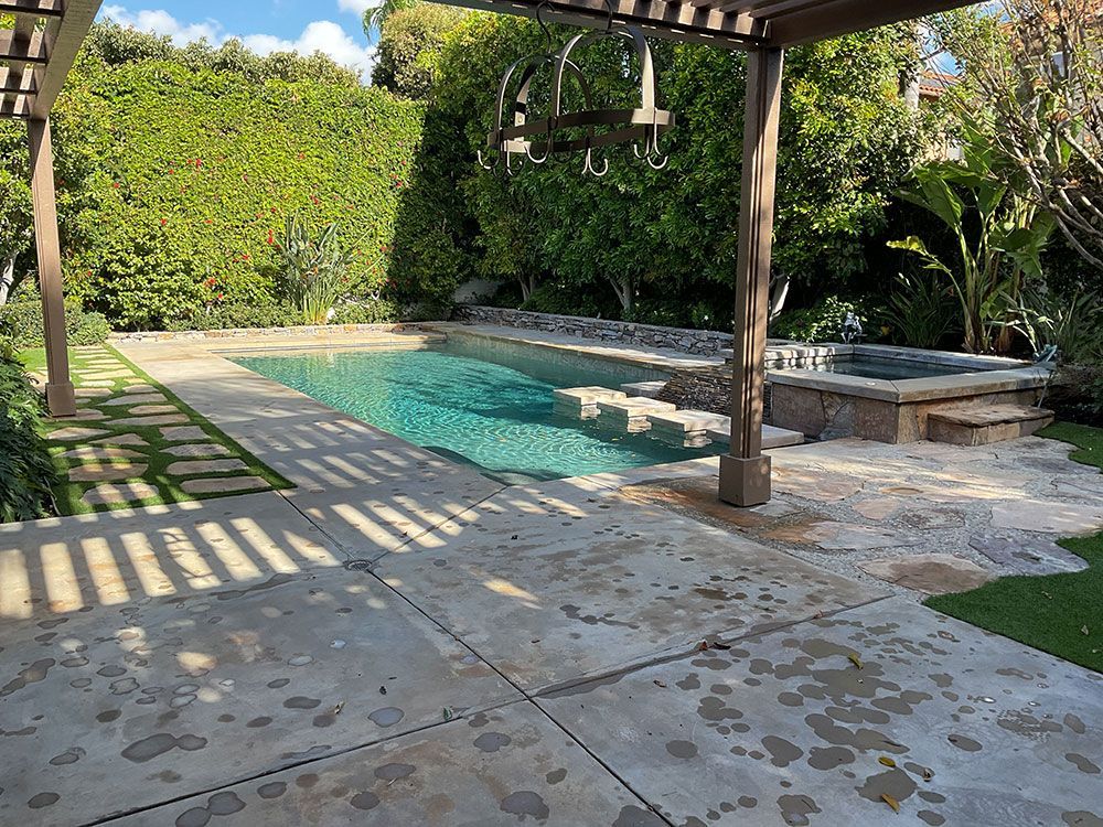 Swimming pool and spa surrounded by greenery and a patio with pergola.