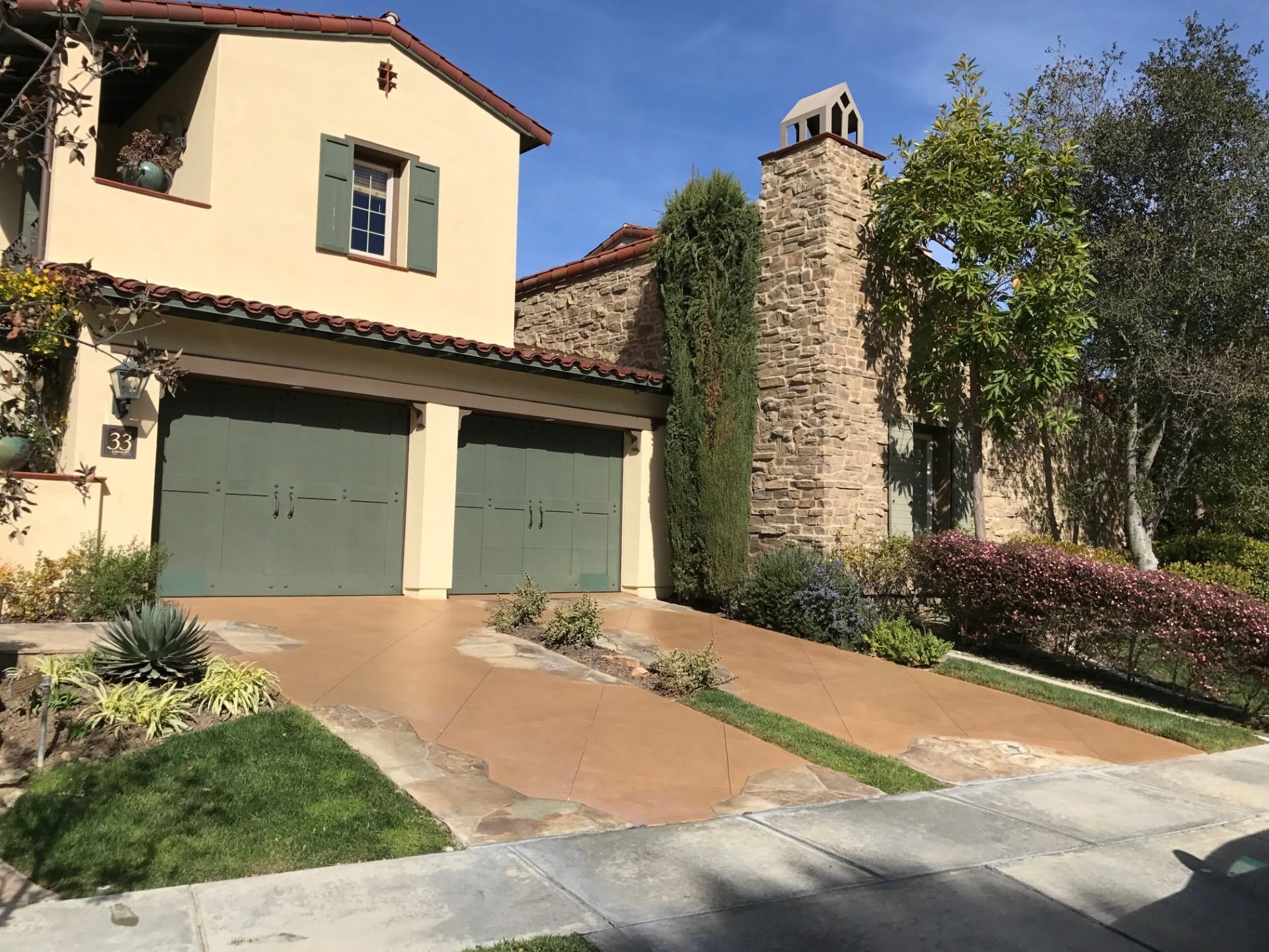 Beige house with green garage doors, stone chimney, and tan driveway.