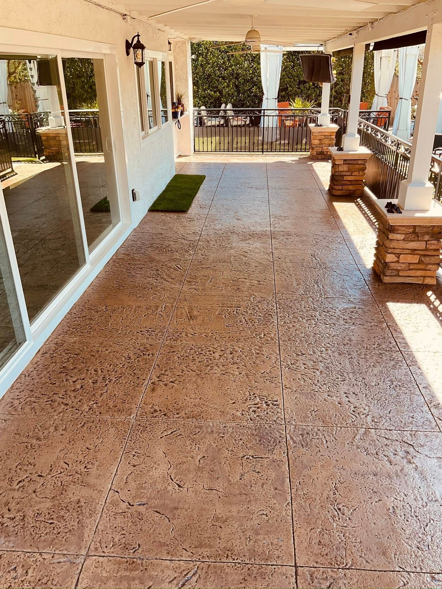 Patio with stamped concrete flooring, covered by a white pergola. The space features columns and glass doors.